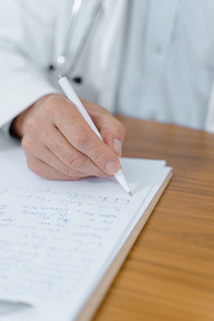 A close-up of a doctor's hand writing notes with a ballpen on paper.