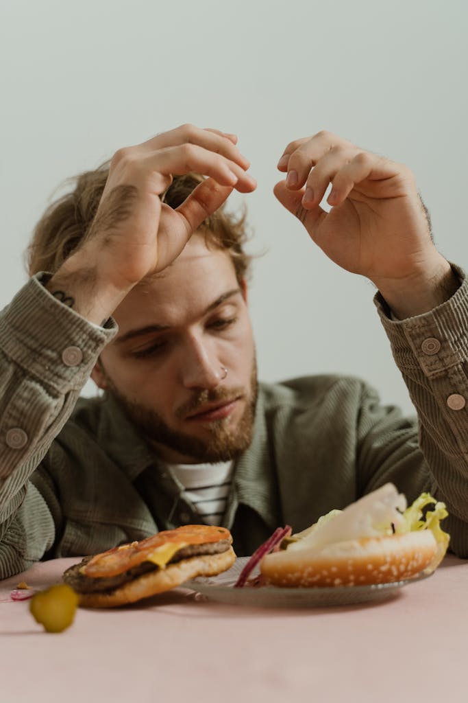 A bearded man in casual attire is looking at a deconstructed hamburger on a table.